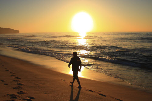 photo of man walking on beach at sunrise